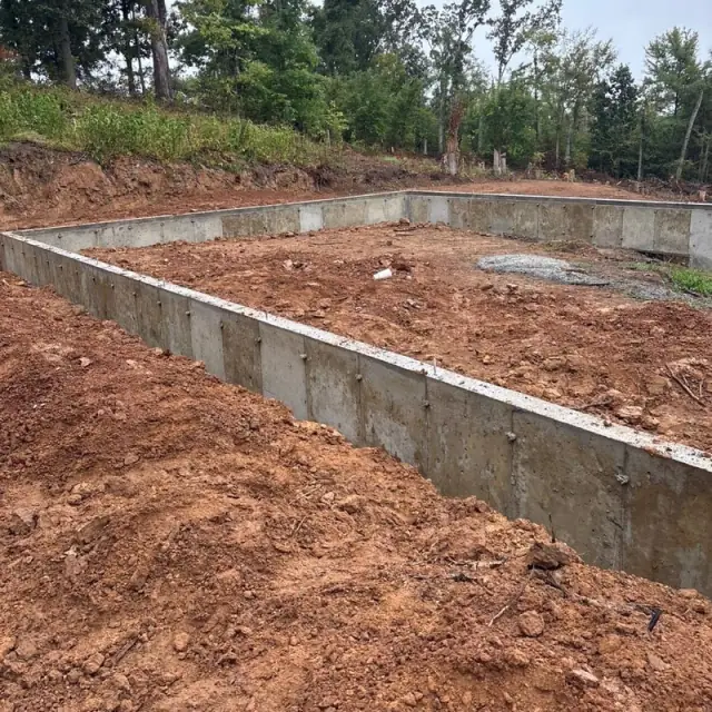 Finished foundation walls set into red clay at the edge of the woods