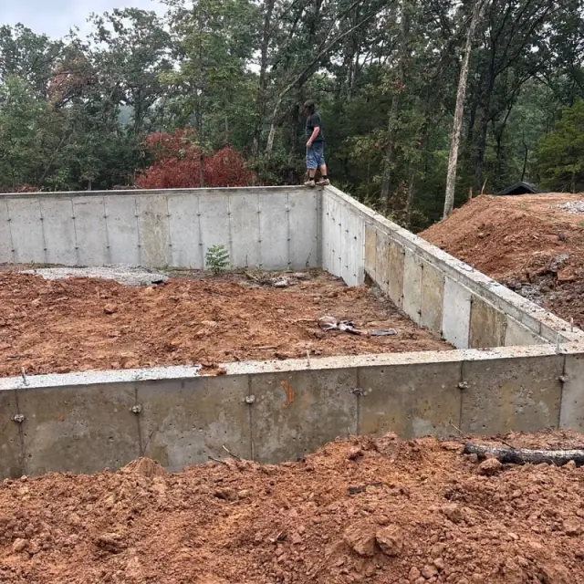 A crew member standing on a finished foundation wall above red clay